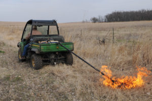 Rancher pulling a drip torch behind an ATV to ignite a prairie burn