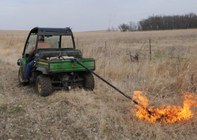 Rancher pulling a drip torch behind an ATV to ignite a prairie burn