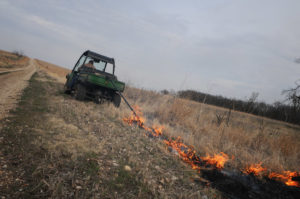 Rancher pulling a drip torch behind an ATV to ignite a prairie burn
