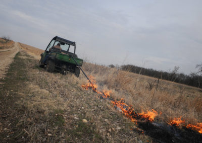 Rancher pulling a drip torch behind an ATV to ignite a prairie burn